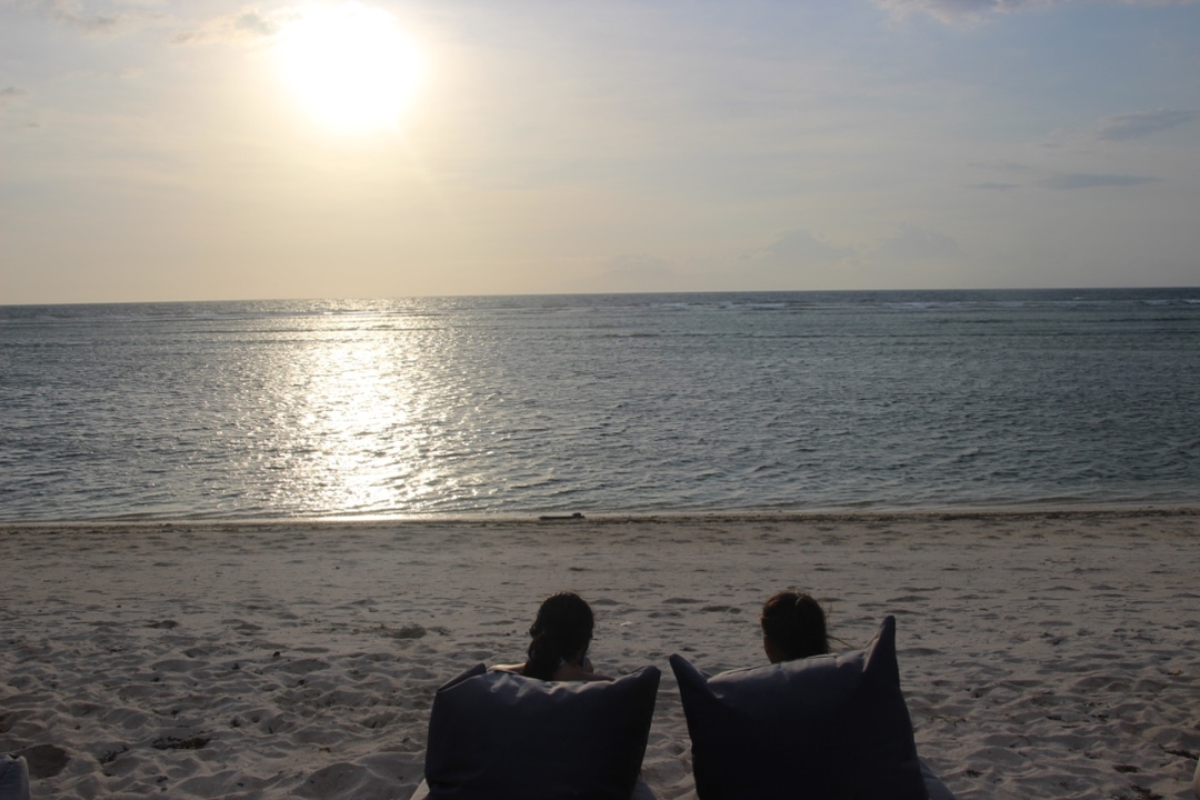 Two people sitting on the beach looking at the ocean during sunset.