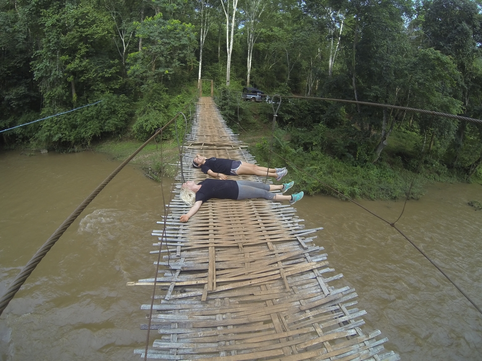 Two people lying on a suspension bridge over a river.