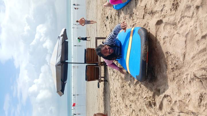Person posing on a beach lounging on a surfboard.