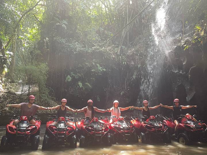 Group of people on ATVs in front of a waterfall.