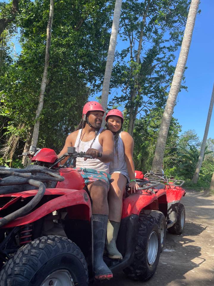 Two people on an ATV in a lush green environment.