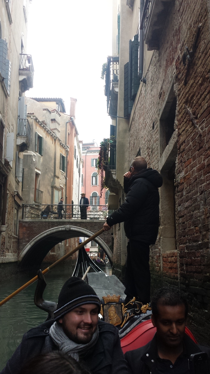 People on a gondola passing under Venetian bridges.