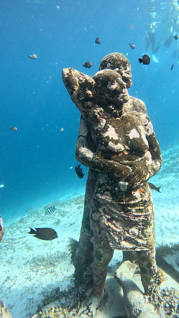 Underwater statue surrounded by fish.