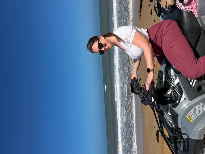 Woman riding an ATV on the beach with waves in the background.