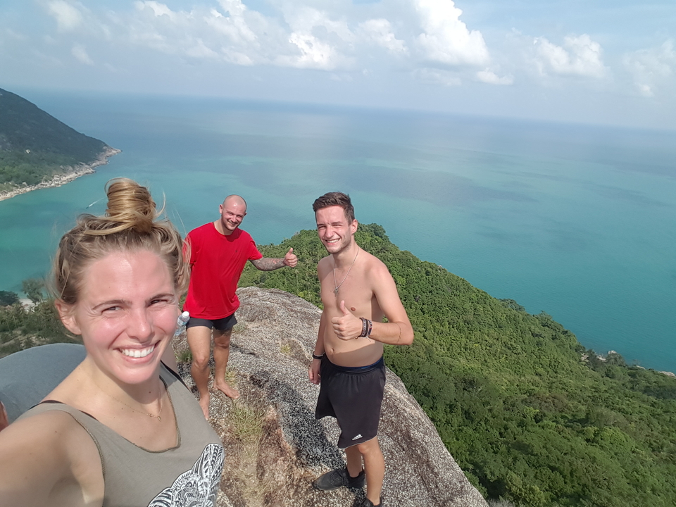 Three people posing on rocky hill with ocean view.