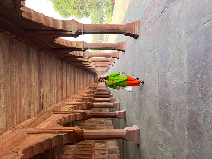 Woman walking down a historic corridor with arches.