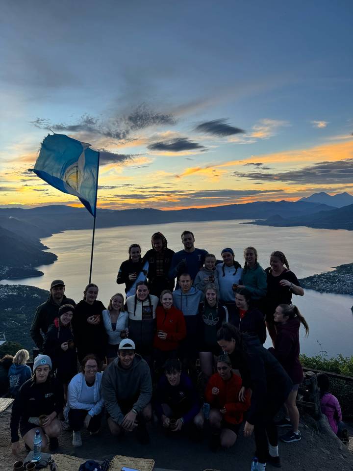 Grand groupe de personnes avec un drapeau au coucher du soleil sur des collines.