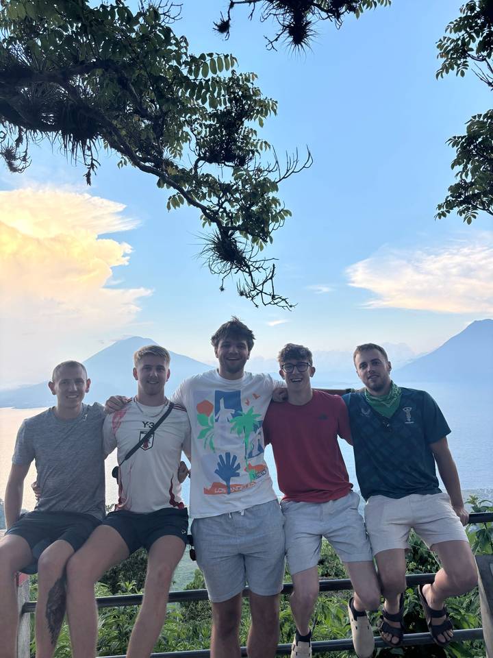 Cinq amis souriants avec un lac et des volcans en arrière-plan.