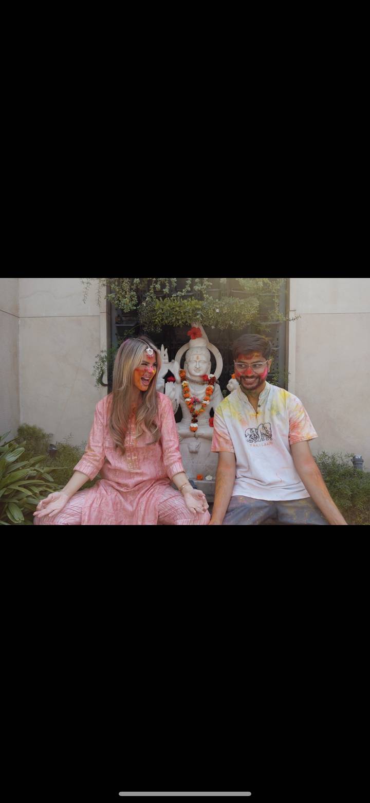 Two people wearing traditional attire with painted faces, statue in the background.
