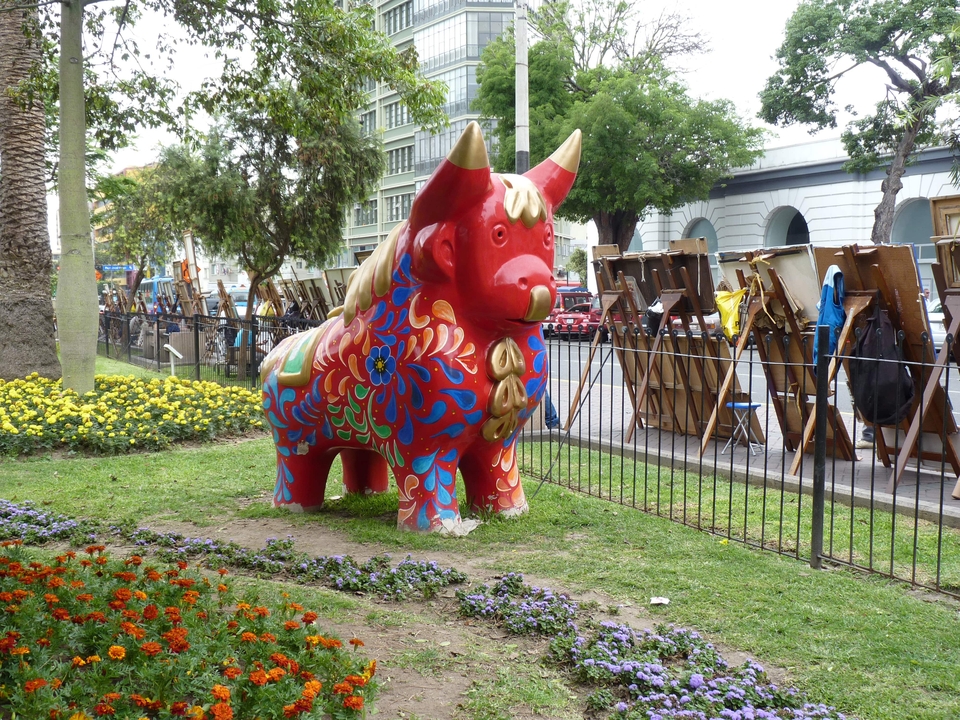 Colorful bull statue in a park with people painting outdoors.
