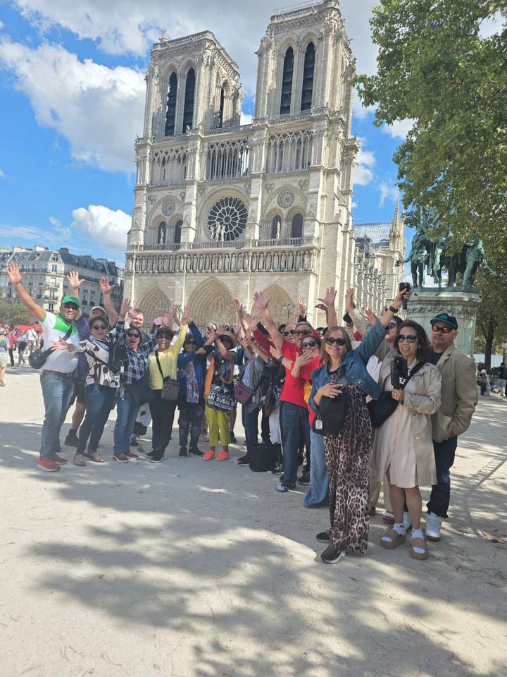 Tourists posing in front of a large cathedral, cheering and smiling.