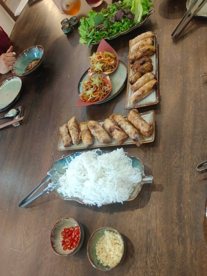 A table with spring rolls, noodles, and vegetables.