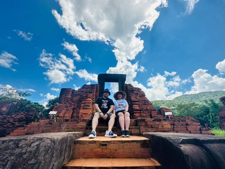 Couple sitting in front of ancient brick ruins under a blue sky.