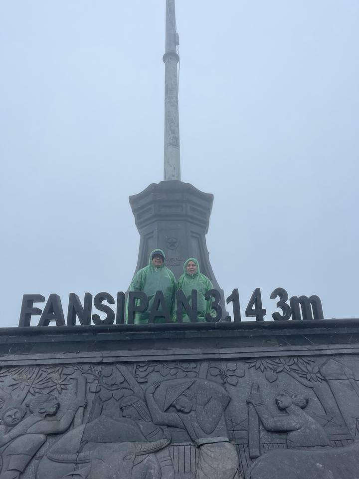 Two people in rain gear at a mountain peak with a sign.