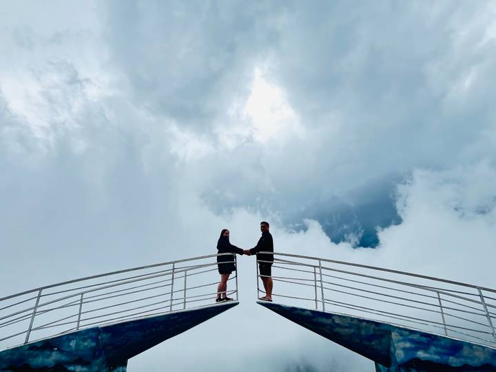 Couple standing on a high platform with clouds in the background.