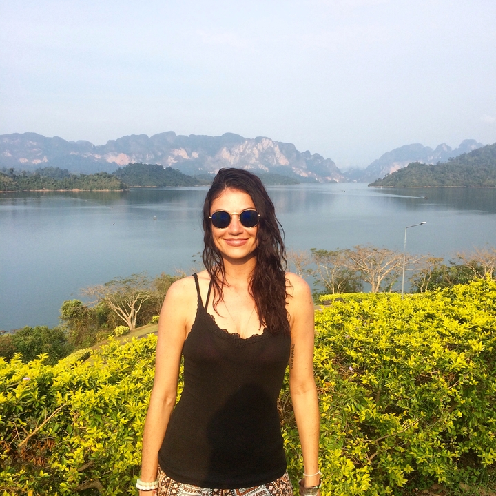 Individual posing with sunglasses in front of a lake and hills.
