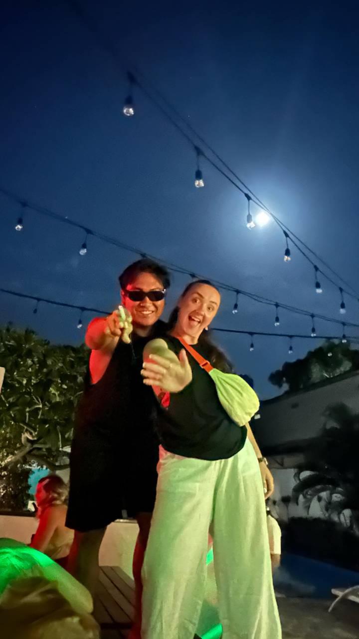 Two people posing together at night under string lights.