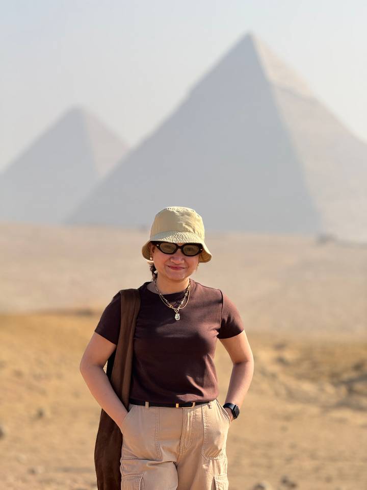 Persoon die voor piramides staat met een hoed en zonnebril op.