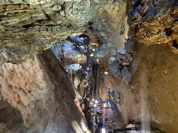 Spacious cave interior with dramatic lighting and visitors exploring.