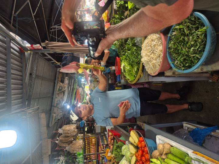 Marktkoopman die producten toont aan een bezoeker tijdens een levendige marktdag.