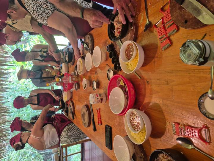 Groepskookles met deelnemers die eten bereiden aan een houten tafel.