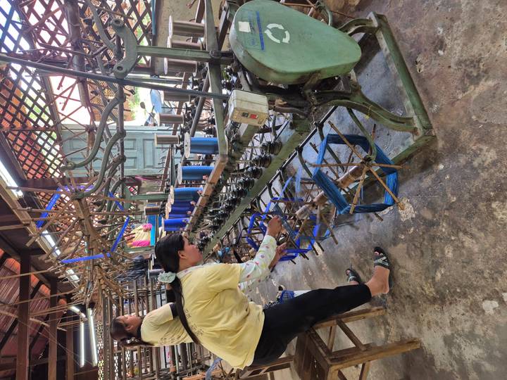 Persoon die werkt met een weefmachine in een textielfabriek.