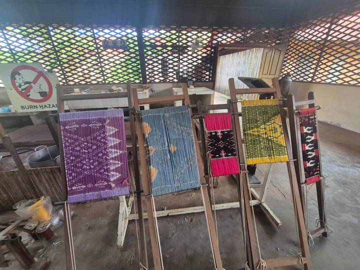 Kleurrijke geweven textiel tentoongesteld met een bord dat waarschuwt voor gevaar.