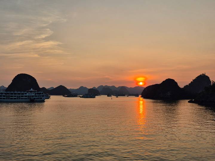 Zonsondergang boven Halong Bay met boten en kalksteenformaties.