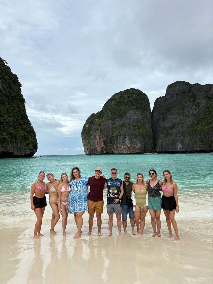 Group photo on a beach with rocky cliffs in the background.