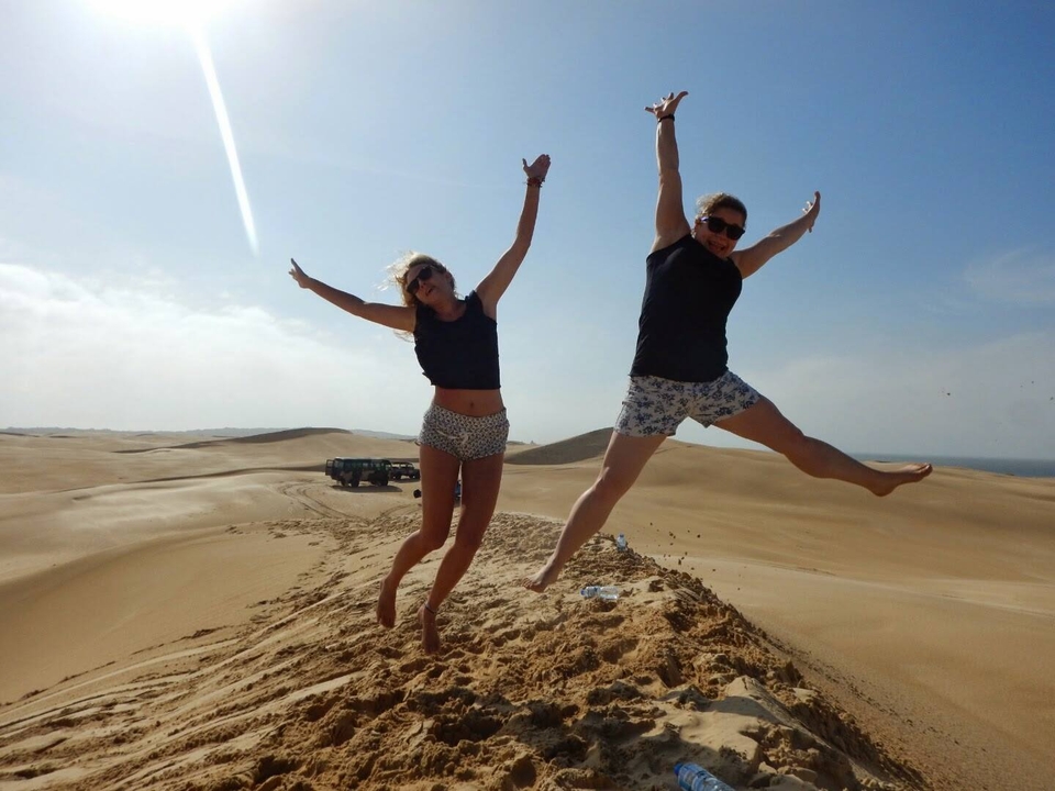 Two people jumping in excitement on sandy dunes.