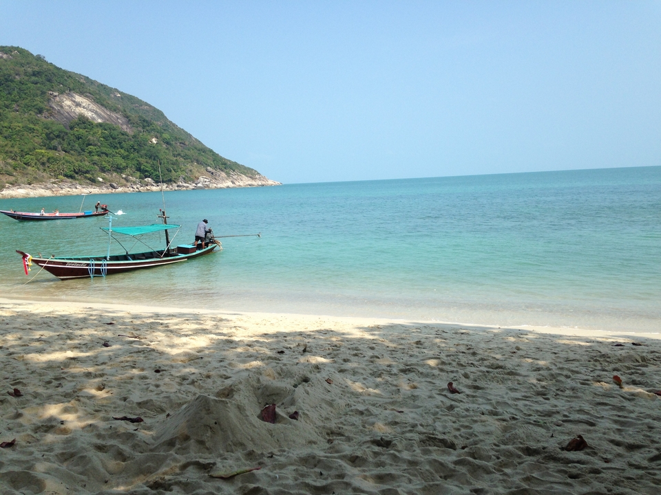 Longtail boat on a sandy beach with turquoise water.