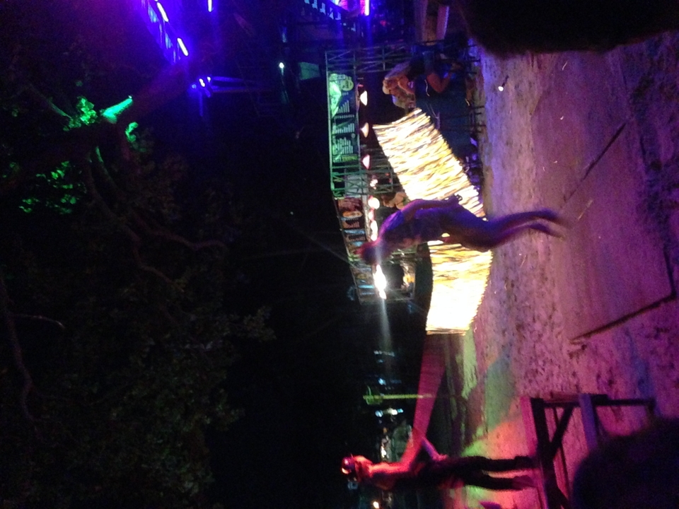 Person standing on a beach at night with vibrant lights in the background.
