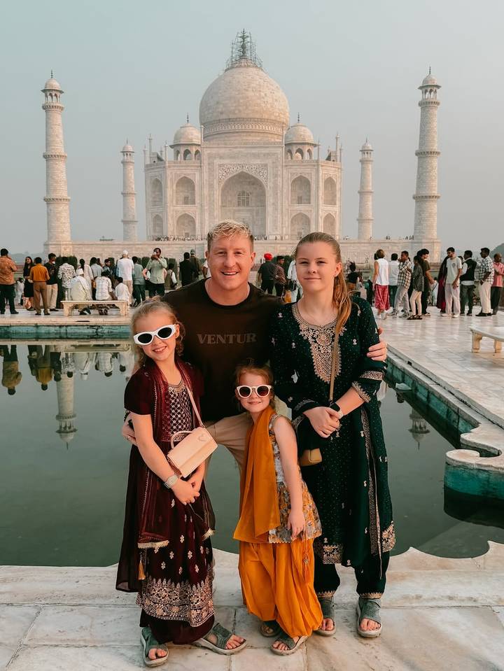 Une famille posant devant un bassin réfléchissant avec le Taj Mahal en arrière-plan.