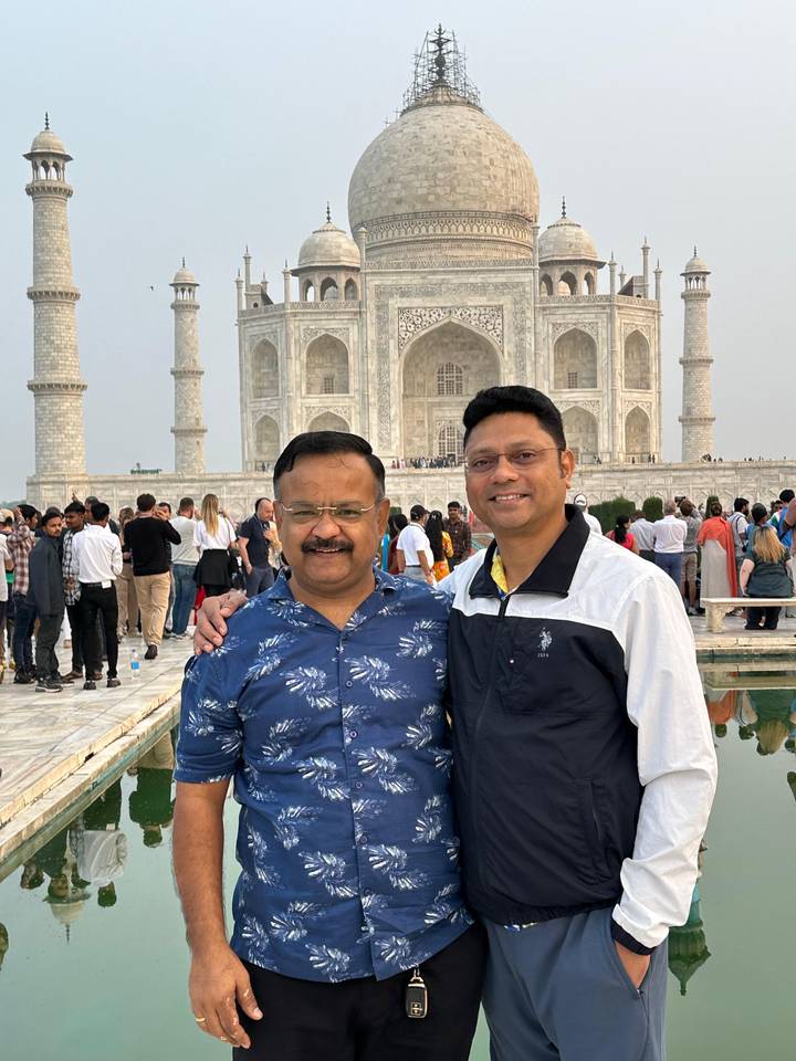 Twee mannen glimlachend voor de Taj Mahal met een menigte.