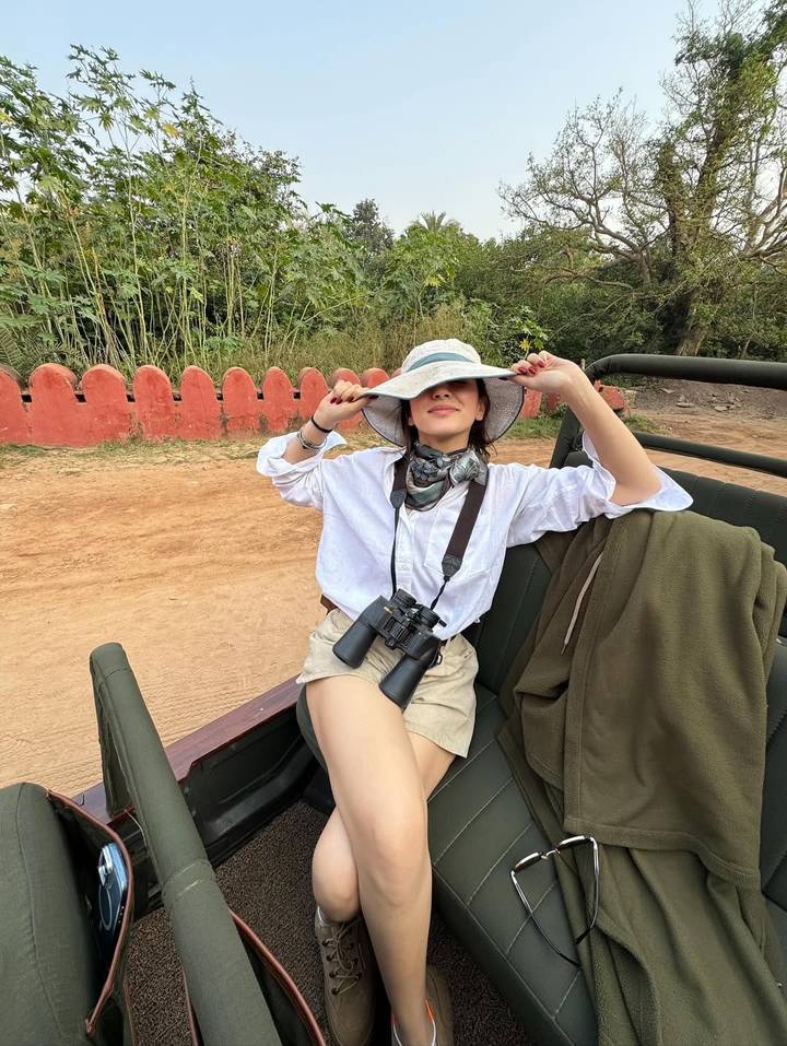 Persoon die in een jeep op safari zit met een hoed op en een verrekijker vasthoudt.