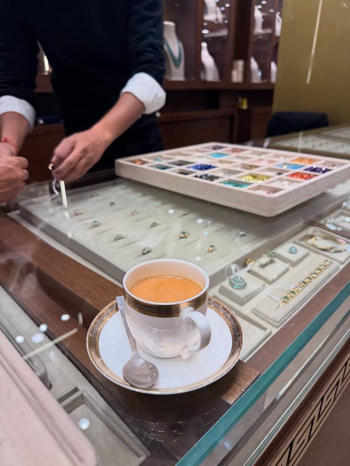 Kopje thee op een toonbank met sieradendisplay en mensen op de achtergrond.