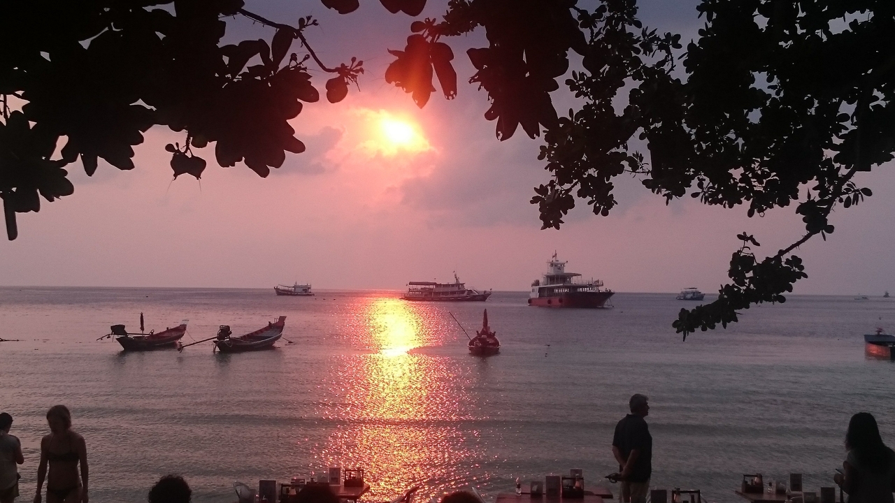 Sunset view with boats and people on the beach.