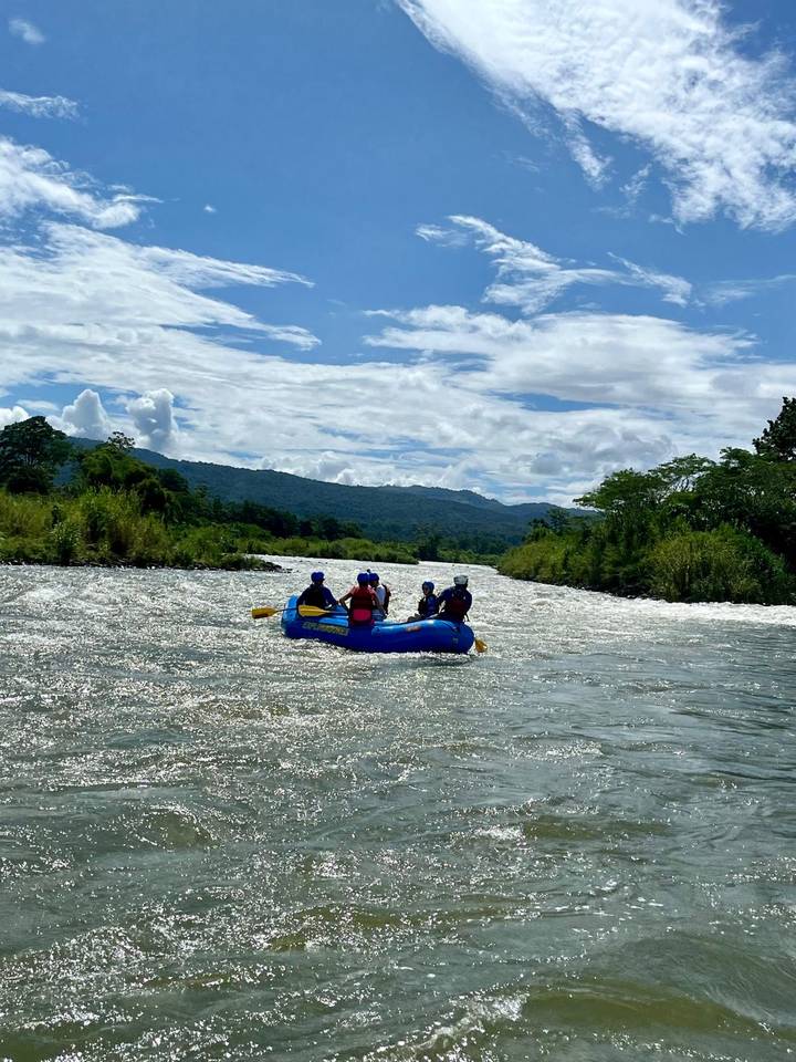 Gruppe von Menschen beim Rafting auf einem Fluss, umgeben von bewaldeten Bergen.