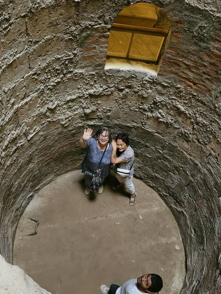 Zwei Personen winken vom Boden eines tiefen Steinbrunnens.