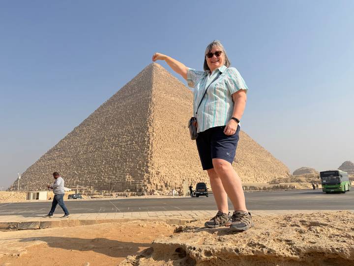 Eine Person posiert mit einer Pyramide im Hintergrund.