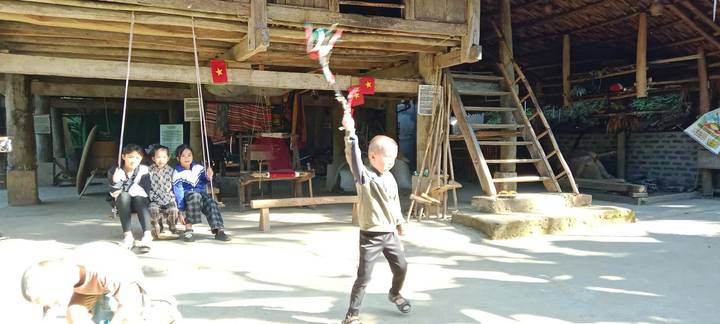 Enfants jouant près d'une maison traditionnelle avec des drapeaux et des décorations.