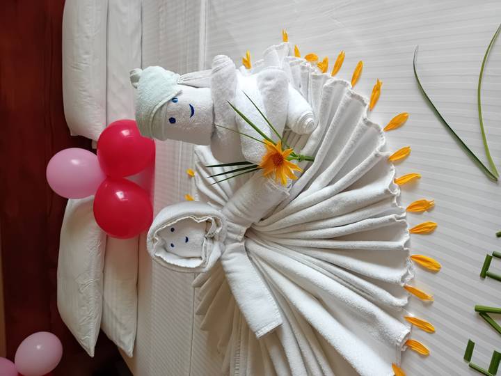 Handdoeksculpturen op een bed met bloemblaadjes en ballonnen erop gerangschikt.