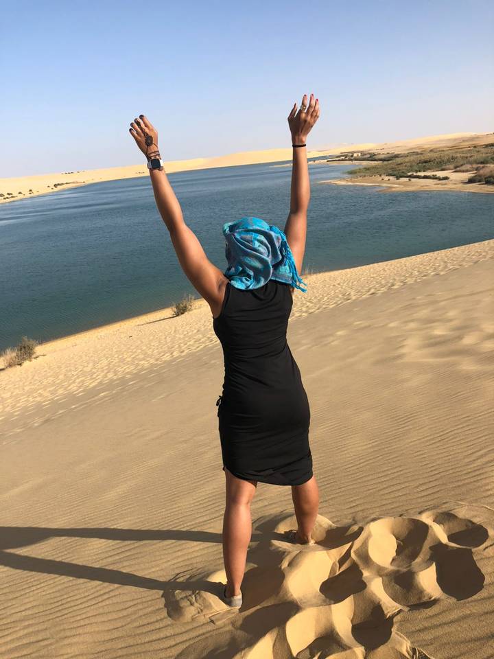 Person mit erhobenen Armen, die auf einer Sanddüne steht.