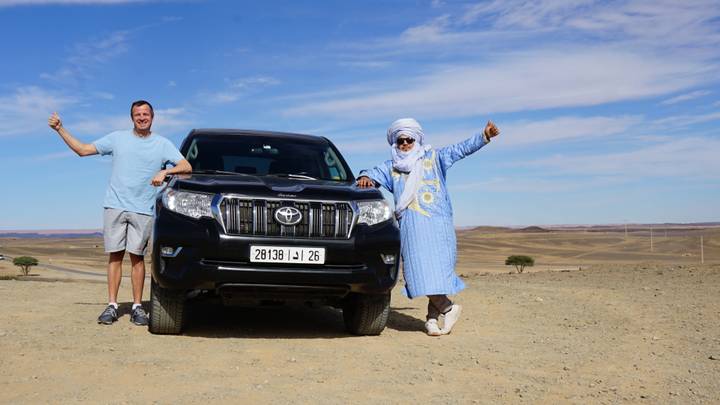 Dos hombres posando frente a un vehículo 4x4 en un desierto.