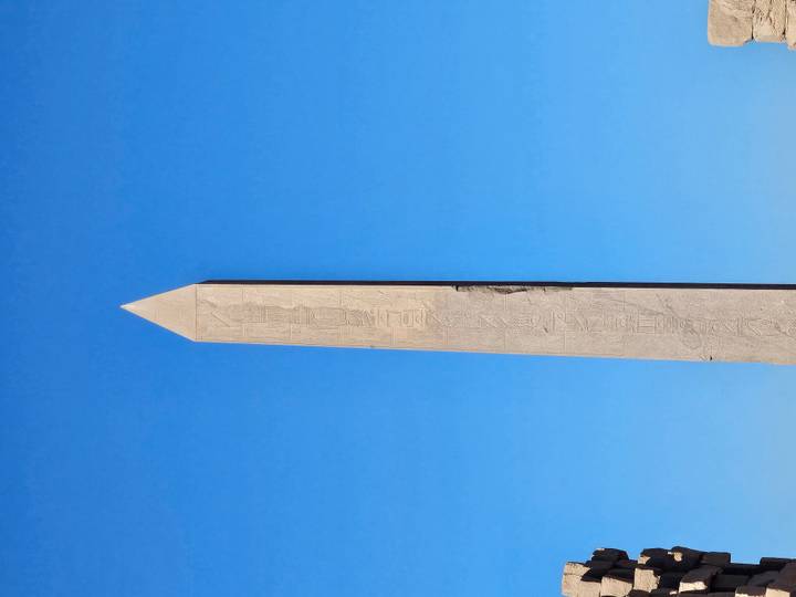Steinobelisk mit Hieroglyphen vor blauem Himmel.
