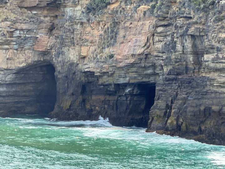 Rotsachtige kustlijn met grotvormingen en groengetint water.