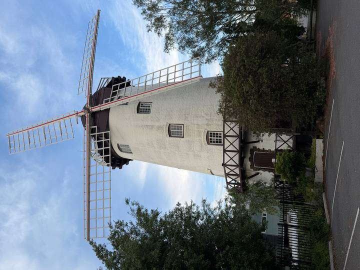 Oude windmolen met roodgetipte wieken tegen een blauwe lucht.