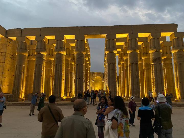 Touristes explorant un grand temple égyptien antique aux colonnes illuminées.