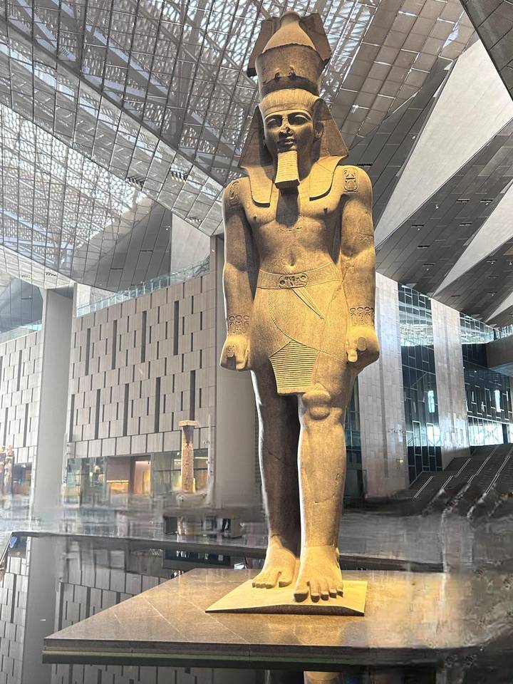 Grande statue égyptienne antique exposée à l'intérieur d'un bâtiment moderne.