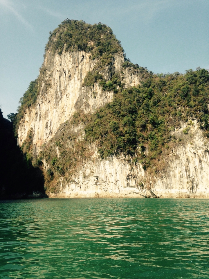 Sheer limestone cliff rising above forested base lit by afternoon light.